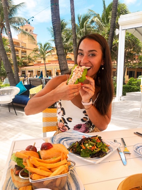 girl eating a lobster roll at the eau palm beach under palm trees next to the pool
