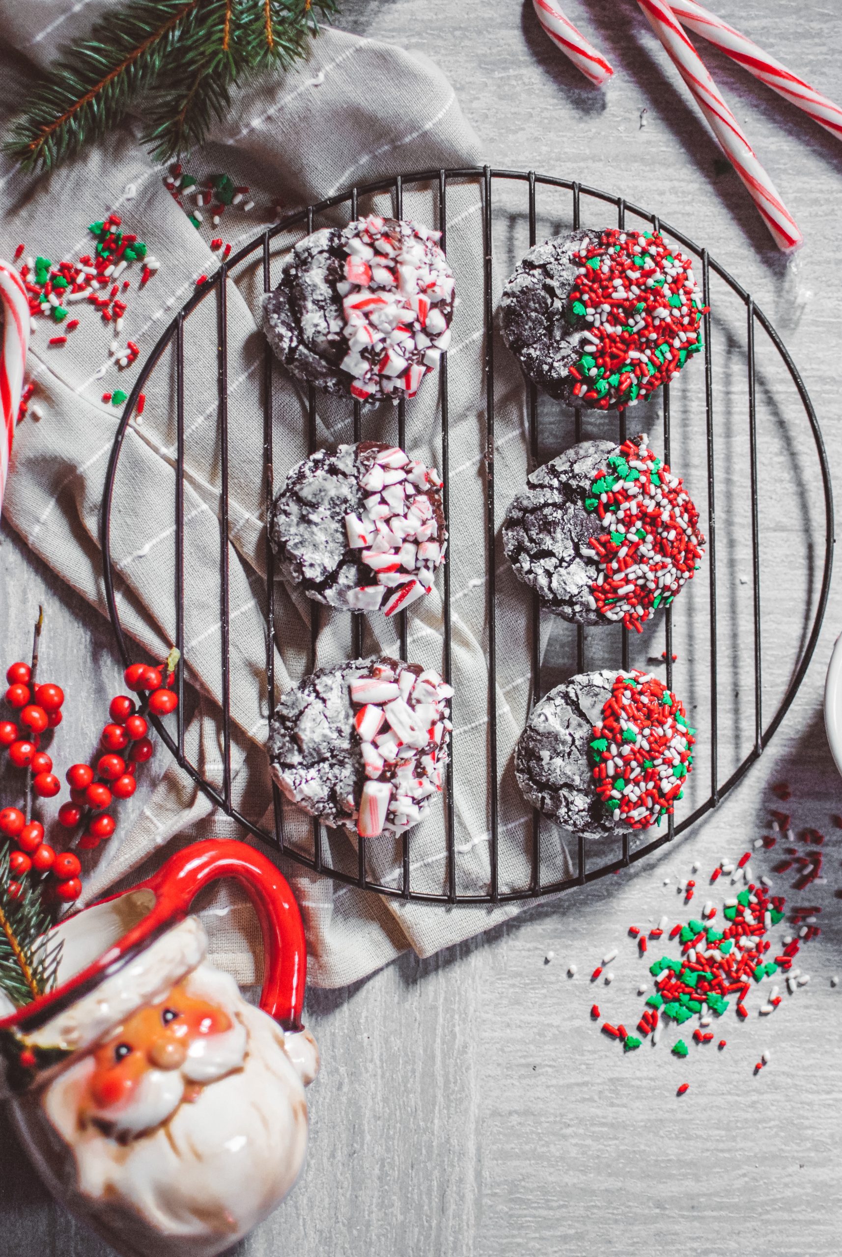 peppermint chocolate crinkle cookies with candy canes, green pine, sprinkles and a santa mug