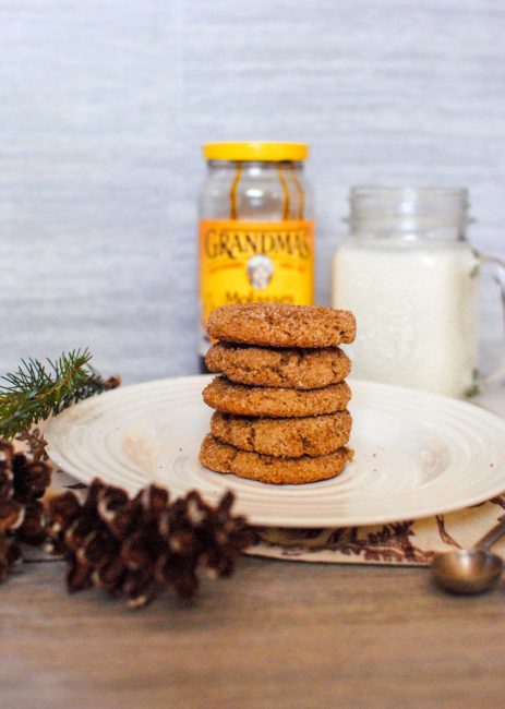 ginger snap cookies surrounded by a glass of milk, pine cones, a white plate and a jar of grandmas molasses